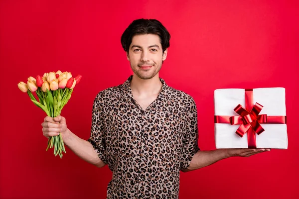 Foto de novio coqueta joven sonriente coqueta dar regalo de San Valentín caja sorpresa tulipanes aislados sobre fondo de color rojo — Foto de Stock