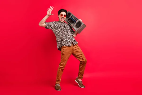 Full size foto van funky achteloos lachende man dansen dolblij hold boombox schouder geïsoleerd op rode kleur achtergrond — Stockfoto