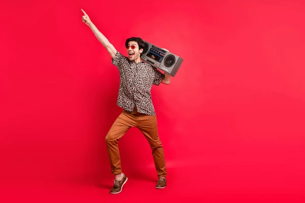 Foto in voller Größe von jungen gut aussehenden aufgeregten verrückten Kerl tanzen mit Boombox Zeigefinger Kopierraum isoliert auf rotem Hintergrund — Stockfoto