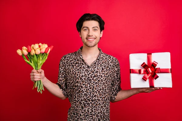 Foto de joven alegre sonriente buen humor guapo macho dar regalo de San Valentín aislado sobre fondo de color rojo — Foto de Stock