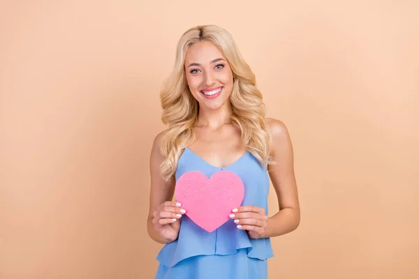Foto wanita muda yang manis manis mengenakan tank-top biru memegang hati merah muda tersenyum latar belakang warna krem terisolasi — Stok Foto