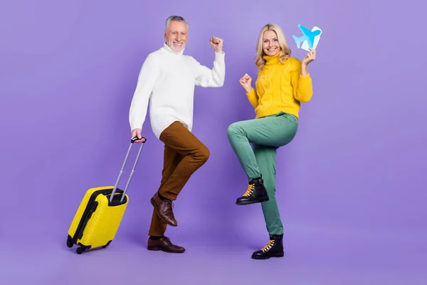 Фотографія досить щасливого старшого чоловіка, дружина одягнена в трикотажні светри, що тримають багаж, піднімаються кулаками, посміхаючись ізольованому фіолетовому кольоровому фоні — стокове фото