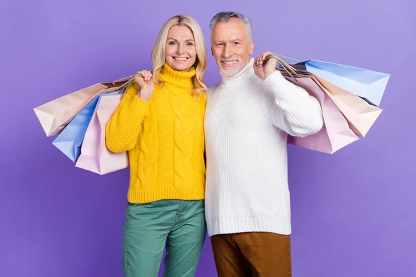 甜美闪亮的成熟妻子丈夫身穿针织套头衫，微笑着抱着购物者孤零零的紫色背景 — 图库照片