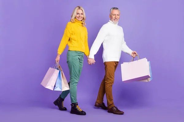 Foto de lindo encantador esposo mayor esposa vestida de punto suéteres caminando sosteniendo los brazos día de compras aislado color violeta fondo — Foto de Stock