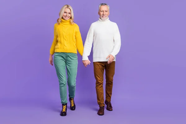 Foto de bastante divertido marido mayor esposa vestida de punto suéteres caminando sosteniendo los brazos sonriendo aislado violeta color de fondo — Foto de Stock