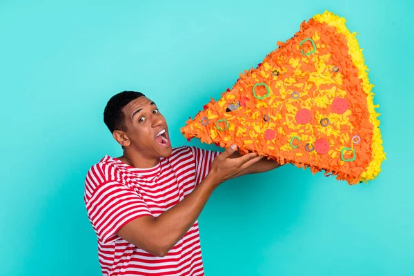 Φωτογραφία του funky αστείο νεαρός άνδρας φορούν ριγέ t-shirt χαμογελώντας δάγκωμα τεράστια πίτσα φέτα απομονωμένη teal φόντο χρώμα — Φωτογραφία Αρχείου