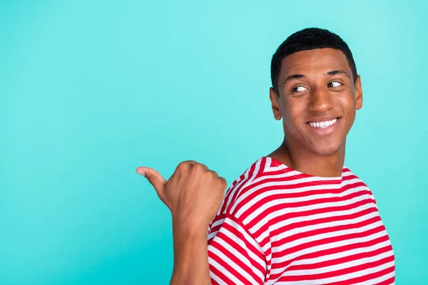 Fotografie okouzlující snivé mladý chlap oblečený červené tričko při pohledu ukazující palec zpět prázdný prostor s úsměvem izolované tyrkysové barvy pozadí — Stock fotografie