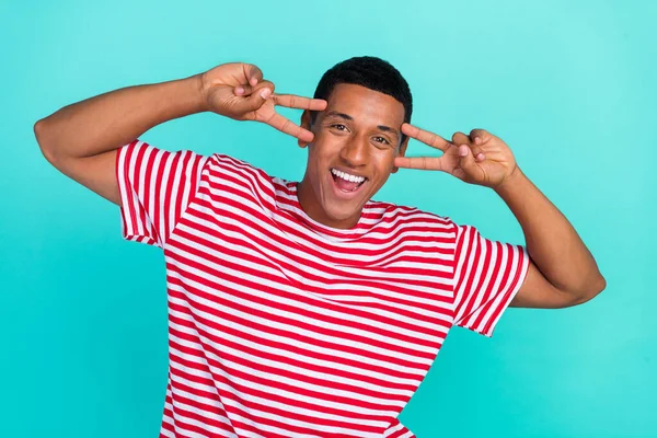 Foto de un joven emocionado de ensueño que usa una camiseta a rayas sonriente que muestra dos signos de v que cubren los ojos, fondo de color verde azulado aislado — Foto de Stock