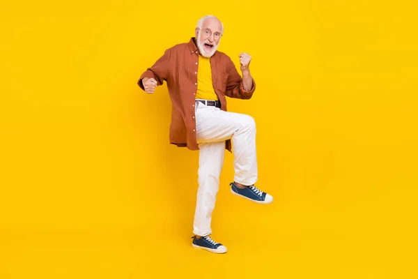 Foto von glücklichen alten Mann heben Hände feiern Sieg tragen Spezifikationen braunes Hemd Hose Schuhe isoliert gelbe Farbe Hintergrund — Stockfoto