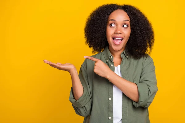 Foto de la curiosa joven morena indican mirada espacio vacío desgaste pantalones vaqueros de color caqui zapatillas aisladas sobre fondo de color amarillo —  Fotos de Stock