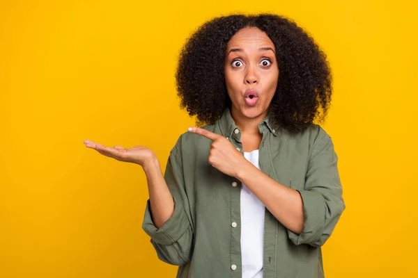 Foto de la morena asombrada millennial lady index espacio vacío desgaste pantalones vaqueros de color caqui zapatillas aisladas sobre fondo de color amarillo —  Fotos de Stock