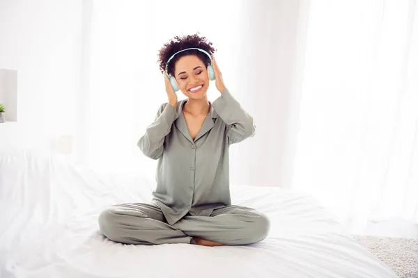 Фото веселих мрій леді сидить ліжко слухати музику блискуча посмішка носити навушники шовковисті сукні в світлій спальні будинку в приміщенні — стокове фото