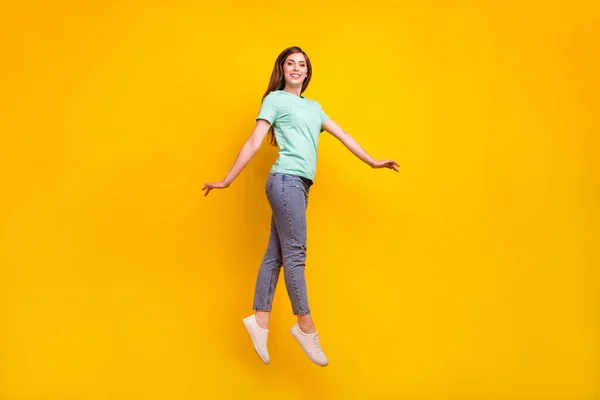 Foto de cuerpo entero de la divertida morena peinado joven dama salto desgaste camiseta jeans zapatillas aisladas sobre fondo amarillo — Foto de Stock