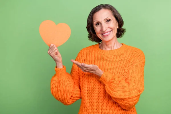 Foto de mulher sênior linda mostrar mão anúncios forma do coração recomendar isolado sobre fundo de cor verde — Fotografia de Stock