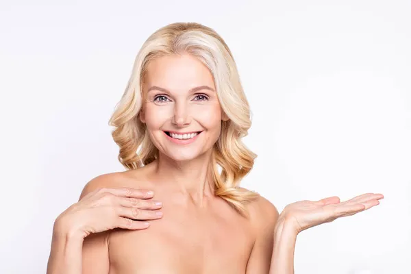 Retrato de atractiva jubilada alegre mujer de pelo gris sosteniendo en copia de la palma anuncio espacio vacío recomiendan aislado sobre fondo de color blanco —  Fotos de Stock