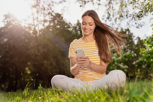 원문 기사보기 몸집 이 큰 여자 가 풀밭에 앉아 스마트폰으로 인터넷을 검색하며 행복하게 웃고 있는 모습 — 스톡 사진