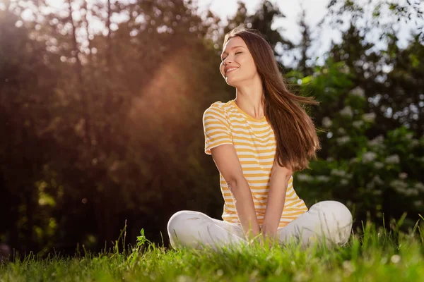 Портрет привабливої веселої дівчини, яка сидить на траві, проводячи вільний час відпочиваючим сонцем, що світить на відкритому повітрі — стокове фото