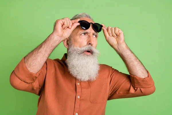 Portrait de séduisant homme aux cheveux gris soupçonneux touchant les spécifications regardant loin isolé sur fond de couleur verte — Photo