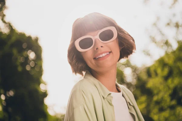 Фото очаровательной милой юной леди, одетой в зеленую рубашку темные очки прогуливаясь улыбаясь на открытом воздухе городской парк — стоковое фото