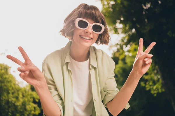 Foto retrato chica joven con el pelo bob en gafas de sol mostrando gesto v-signo en la calle soleada de verano con ropa casual — Foto de Stock