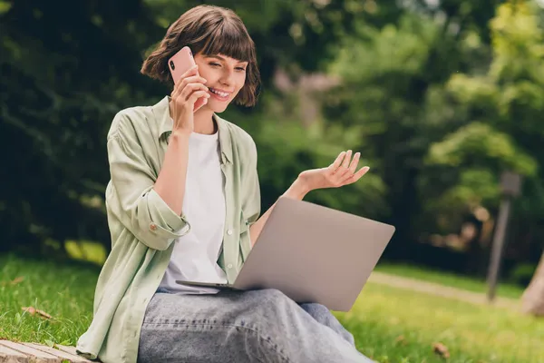 Portrait photo smiling young girl sitting on ground working on laptop browsing internet talking on cellphone — Stock Photo, Image