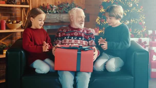Funny family gathering grandfather laugh hold box gift children ask open package — Stock Video