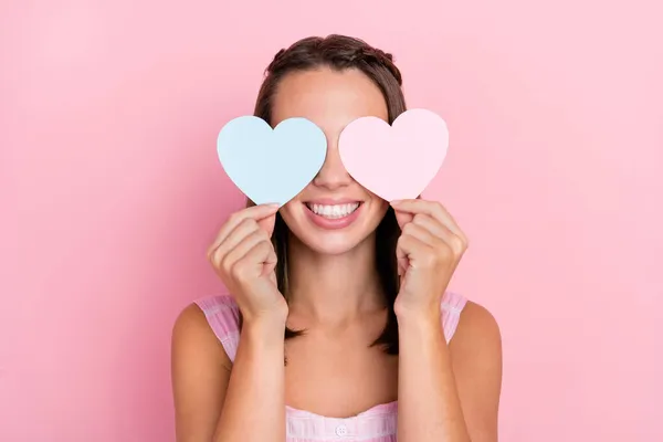 Foto de alegre agradável positiva jovem feliz segurar corações de papel cobrir os olhos isolados no fundo cor-de-rosa — Fotografia de Stock