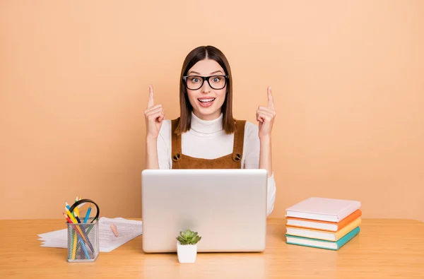 Portret van aantrekkelijke vrolijke meisje werknemer met behulp van laptop wijzen op kopieerruimte oplossing geïsoleerd over beige kleur achtergrond — Stockfoto