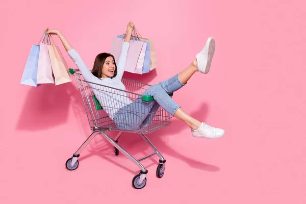 Foto van zoete onder de indruk jonge dame gekleed witte trui rijzende tassen paardrijden winkelwagen trolley geïsoleerde roze kleur achtergrond — Stockfoto