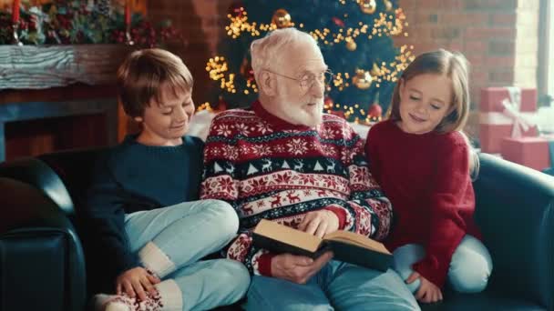 El abuelo inteligente positivo sostiene el libro lea la historia de x-mas de los niños — Vídeo de stock