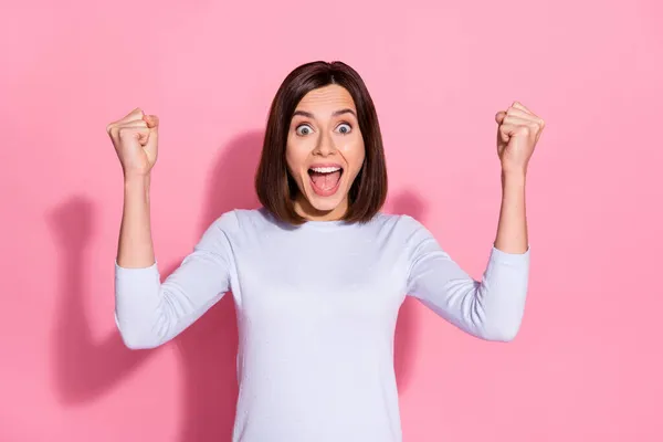 Foto de mujer joven bastante afortunada usar suéter blanco levantando puños gritando ganar jackpot aislado color rosa fondo —  Fotos de Stock