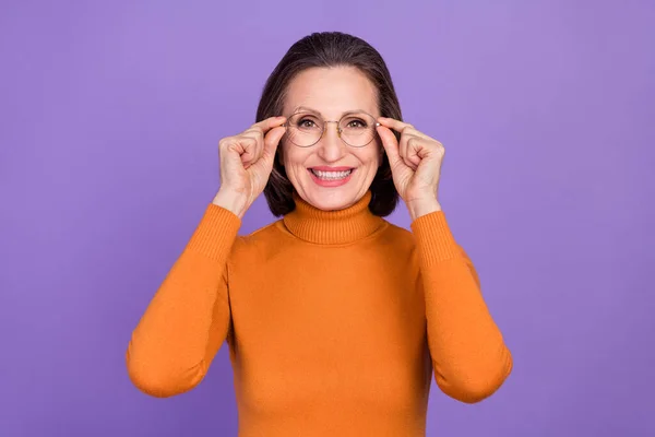 Foto di affascinante carino signora pensionato vestito arancione dolcevita braccia occhiali sorridente isolato colore viola sfondo — Foto Stock