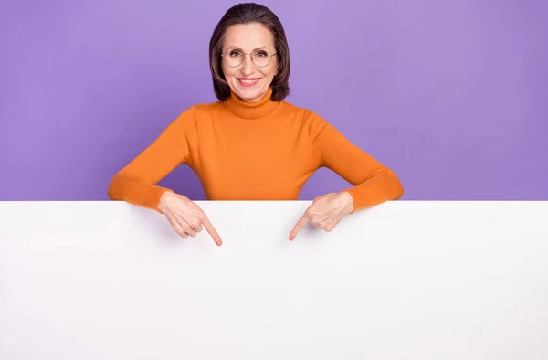 Foto von süßen entzückenden Rentnerin tragen orangefarbenen Pullover Brille zeigt weiße Poster leeren Raum isoliert violette Farbe Hintergrund — Stockfoto