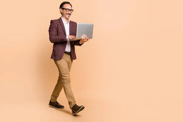 Full length body size view of attractive cheerful man going using laptop copy space isolated over beżowy kolor tła — Zdjęcie stockowe