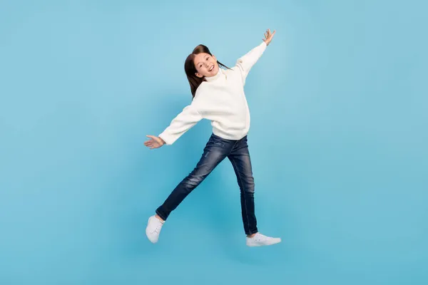 Foto de menina pré-adolescente doce animado vestido pulôver branco pulôver pulando lados de braços altos sorrindo isolado fundo de cor azul — Fotografia de Stock