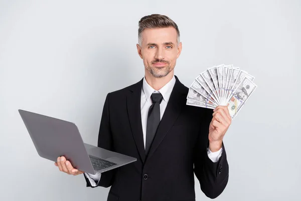 Foto van knappe zelfverzekerde volwassen broker gekleed zwart pak werken moderne gadget met dollars ventilator geïsoleerde grijze kleur achtergrond — Stockfoto