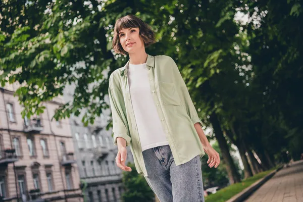 Фото очаровательной мечтательной молодой женщины, одетой в зеленую рубашку, улыбающейся выходящей на улицу города. — стоковое фото