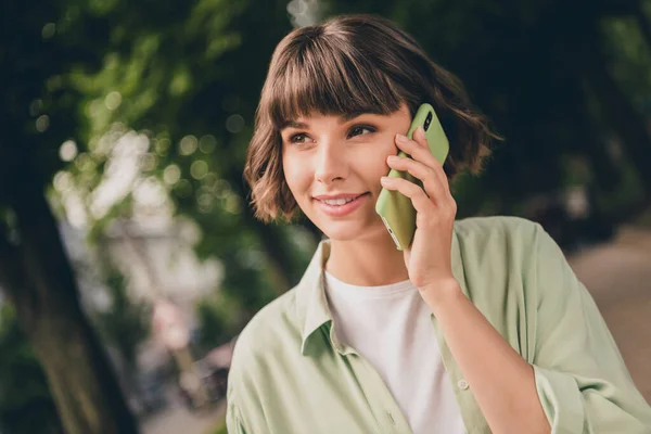 매력적 인 젊은 여성의 사진 녹색 셔츠를 입고 웃으며 도시의 거리 밖에서 현대식 기기를 말하는 모습 — 스톡 사진