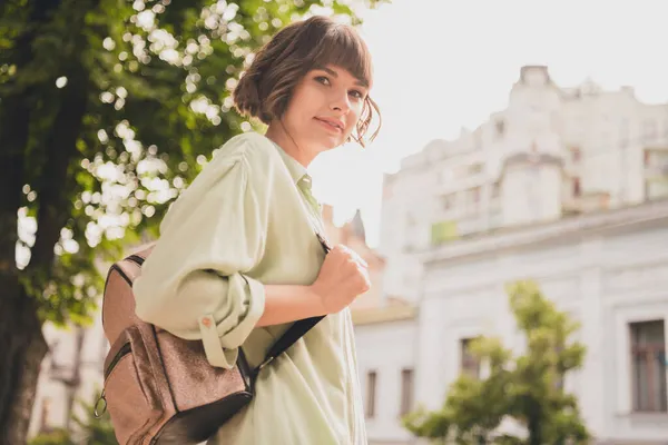 Zdjęcie uroczej młodej kobiety noszącej zielony plecak koszuli uśmiechającej się spacerując poza ulicą miasta — Zdjęcie stockowe