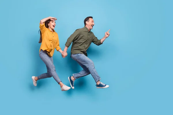 Full size photo of brunette haired husband wife amazed jump run empty space point finger isolated on blue color background — Stock Photo, Image