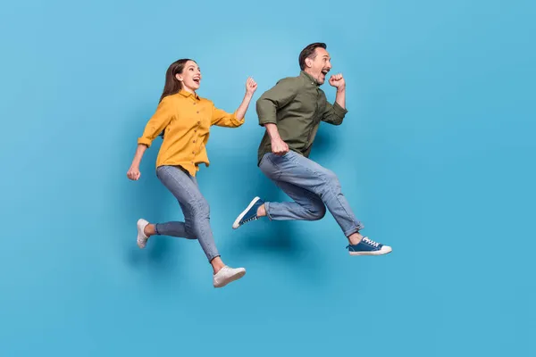 Volledige lengte foto van bruin haar echtgenoot vrouw springen omhoog run lege ruimte verkoop geïsoleerd op pastel blauwe kleur achtergrond — Stockfoto