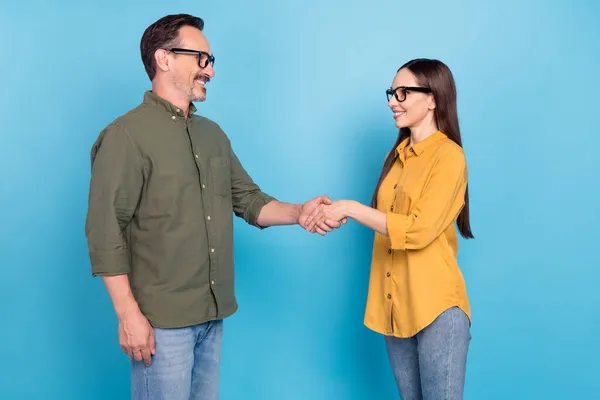 Foto de hombre feliz maduro y la gente de la mujer usan gafas trato apretón de manos aislado en fondo de color azul — Foto de Stock
