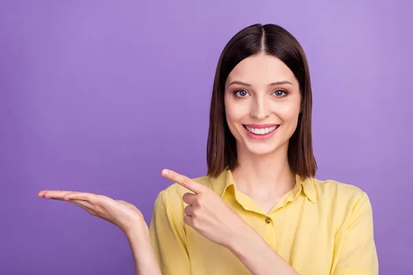 Fénykép a fiatalok szép vidám lány jelzi ujj termék hirdetni elszigetelt felett lila színű háttér — Stock Fotó