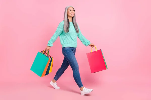Фотографія солодкого білого волосся старша леді робить покупки одягають джинсовий светр взуття для очей ізольовані на рожевому кольорі — стокове фото