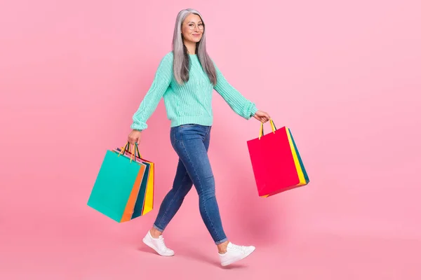 完全な長さ写真のかわいいグレー毛老婦人doショッピング摩耗アイウェアセータージーンズ履物隔離されたピンク色の背景 — ストック写真
