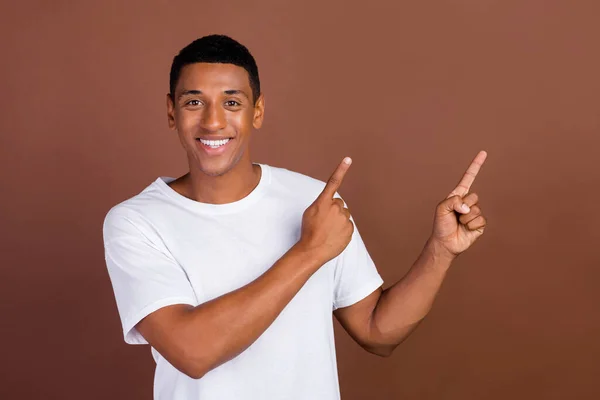 Foto von optimistischen jungen brünetten Kerl Index leeren Raum tragen weißes T-Shirt isoliert auf braunem Hintergrund — Stockfoto