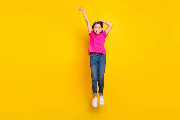 Foto de menina salto mão medida espaço vazio desgaste rosa t-shirt jeans sapatos isolado cor amarela fundo — Fotografia de Stock