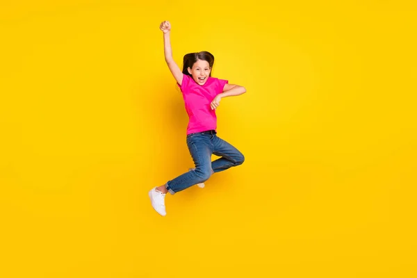 Foto do animado salto menina pequena desfrutar de rodeio cavalo desgaste rosa t-shirt jeans sapatos isolado cor amarela fundo — Fotografia de Stock