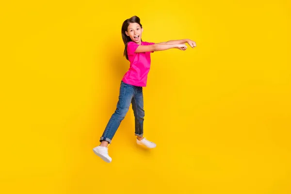 Photo of positive little cowgirl jump pretend ride horse wear pink t-shirt jeans shoes isolated yellow color background