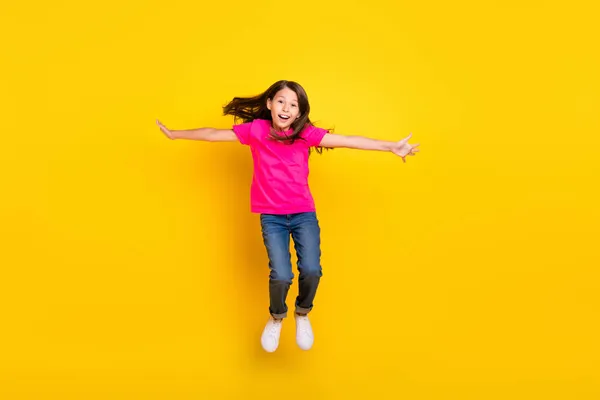 Photo of little girl jump hands wings plane pose flight wear pink t-shirt jeans sneakers isolated yellow color background